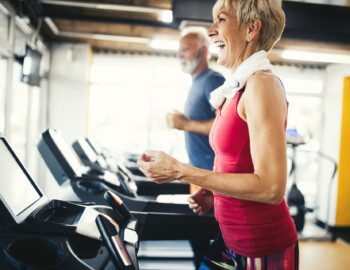 senior woman smiles while walking on the treadmill at her senior fitness center