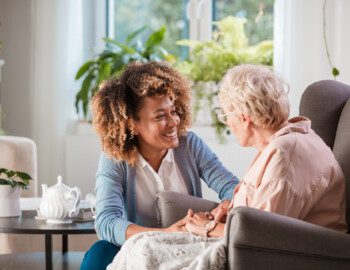 caregiver smiles while helping senior woman who sits in a reclining chair