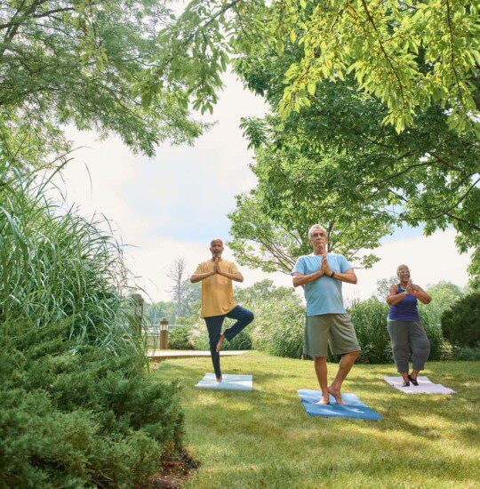 group of three seniors practice yoga poses outside at Oak Trace Senior Living Community