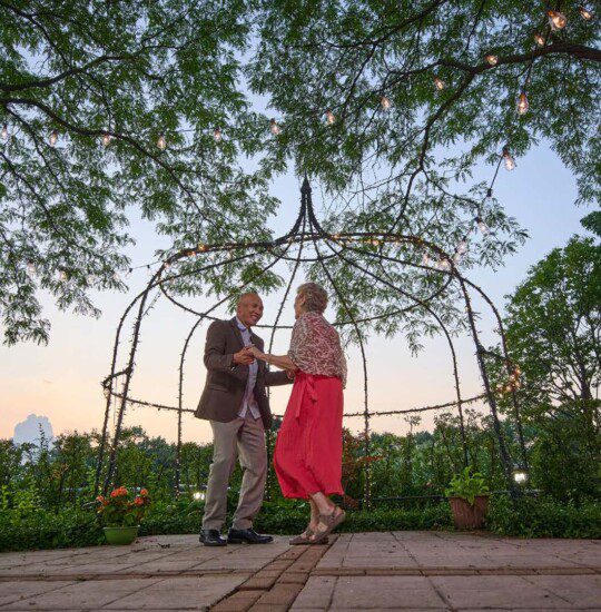 senior couple in elegant clothing dances together outside at sunset under fairy lights at Oak Trace Senior Living Community