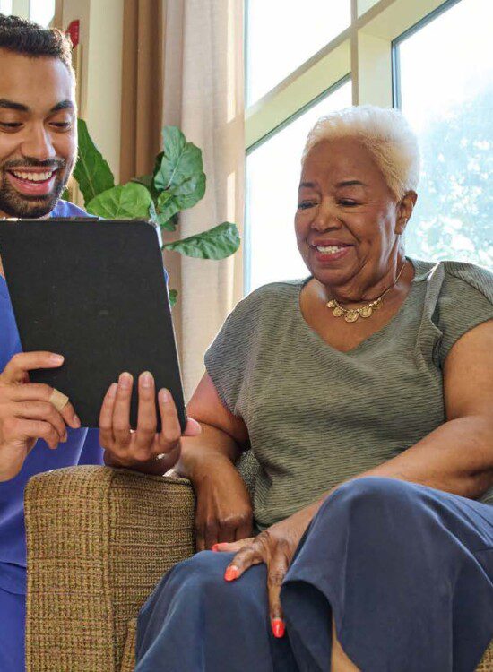 senior woman smiles while sitting in a chair discussing her health plan with a care taker