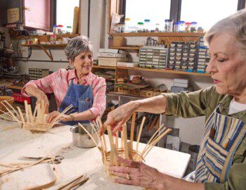 two senior women work on basket weaving at a workshop at Oak Trace Senior Living Community