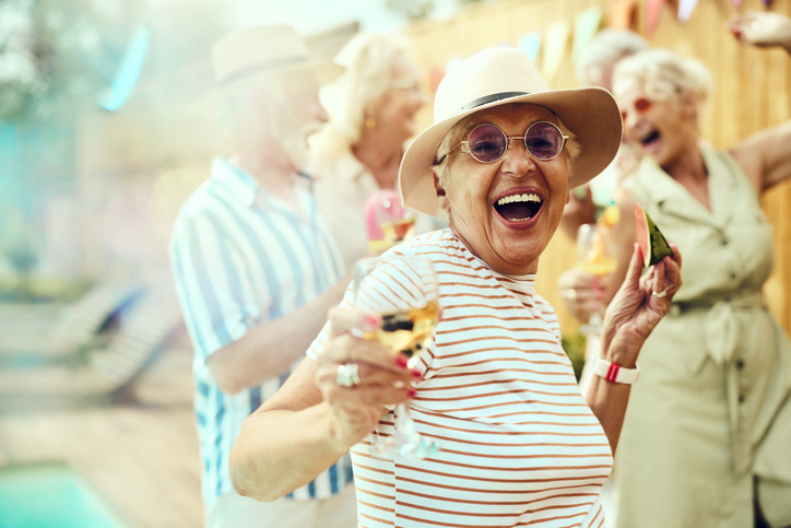 Carefree mature woman having fun with her friends during a summer party by the pool in the backyard and looking at camera.