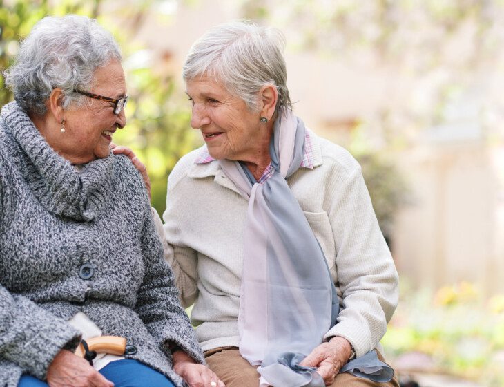 Two elderly women sitting on bench in park smiling happy life long friends enjoying retirement