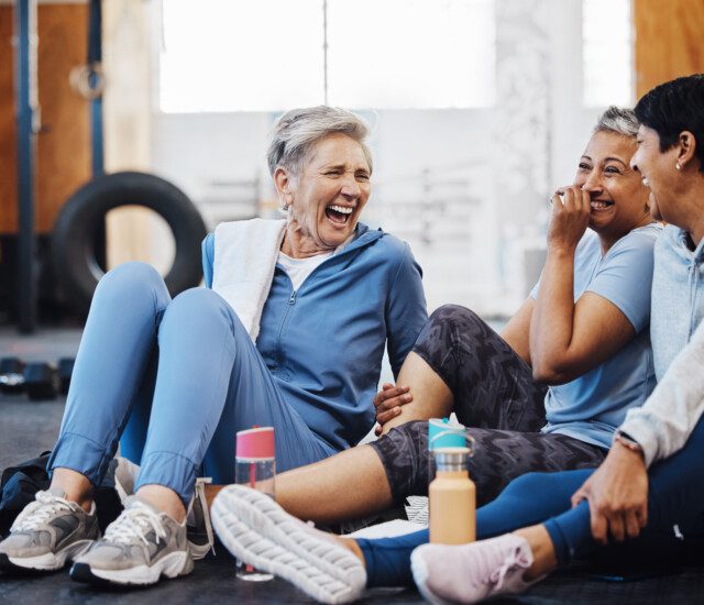 Gym, laughing and group of mature women telling joke after fitness class, conversation and comedy on floor. Exercise, bonding and happy senior woman with friends sitting chatting together at workout.