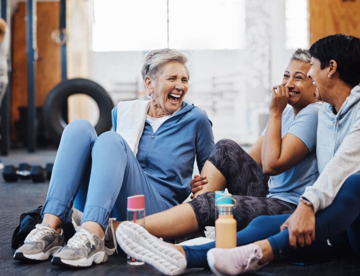 Gym, laughing and group of mature women telling joke after fitness class, conversation and comedy on floor. Exercise, bonding and happy senior woman with friends sitting chatting together at workout.